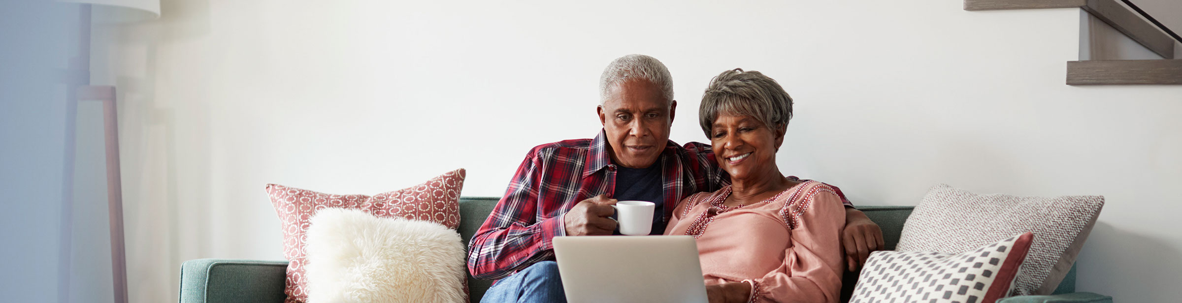 two mature couples sitting on a couch viewing their laptop computer
