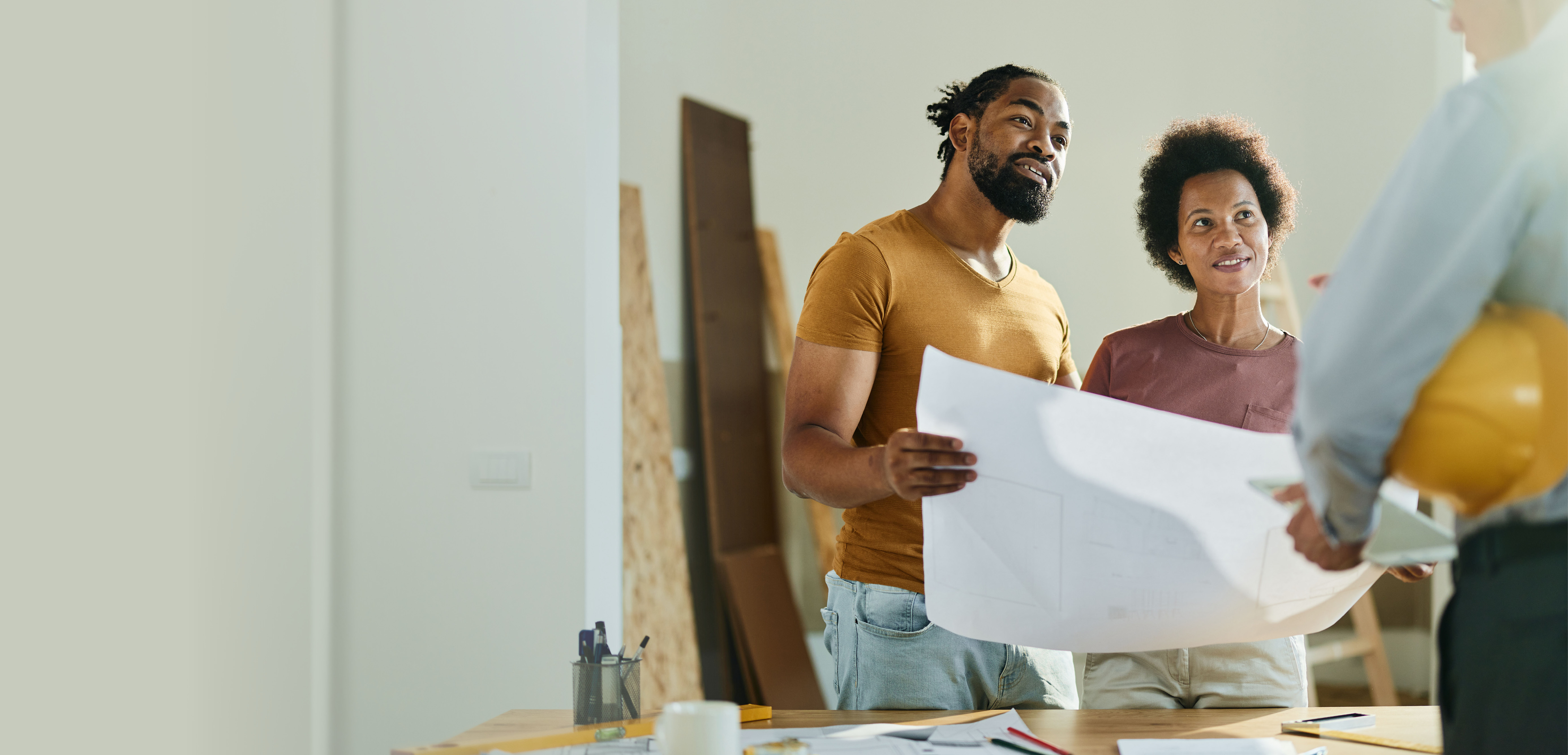 young couple holding blueprint discussing changes with contractor